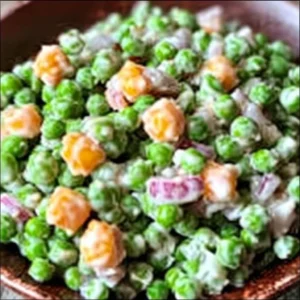 Bowl of classic pea salad featuring fresh peas, cheese, and dressing.